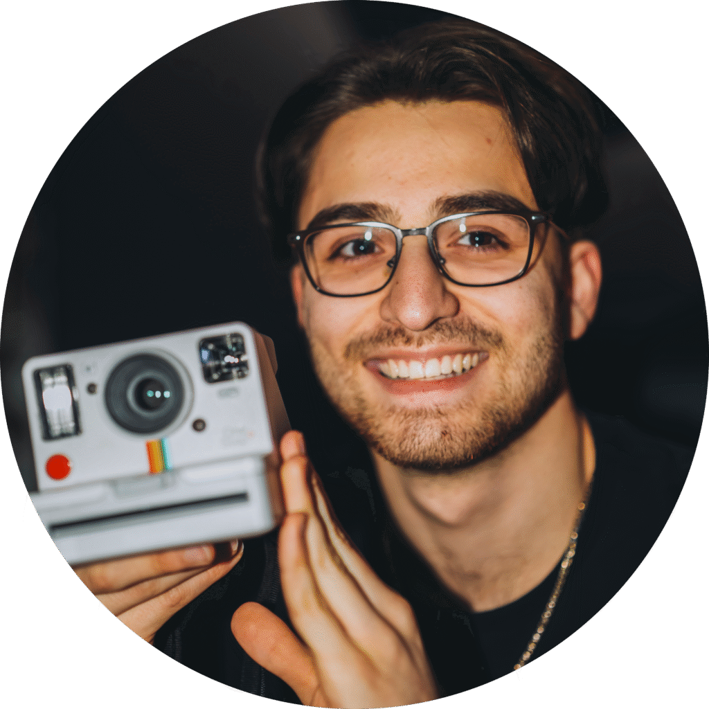 BaranBeatzz lächelt in die Kamera und hält eine klassische Polaroid-Kamera in der Hand