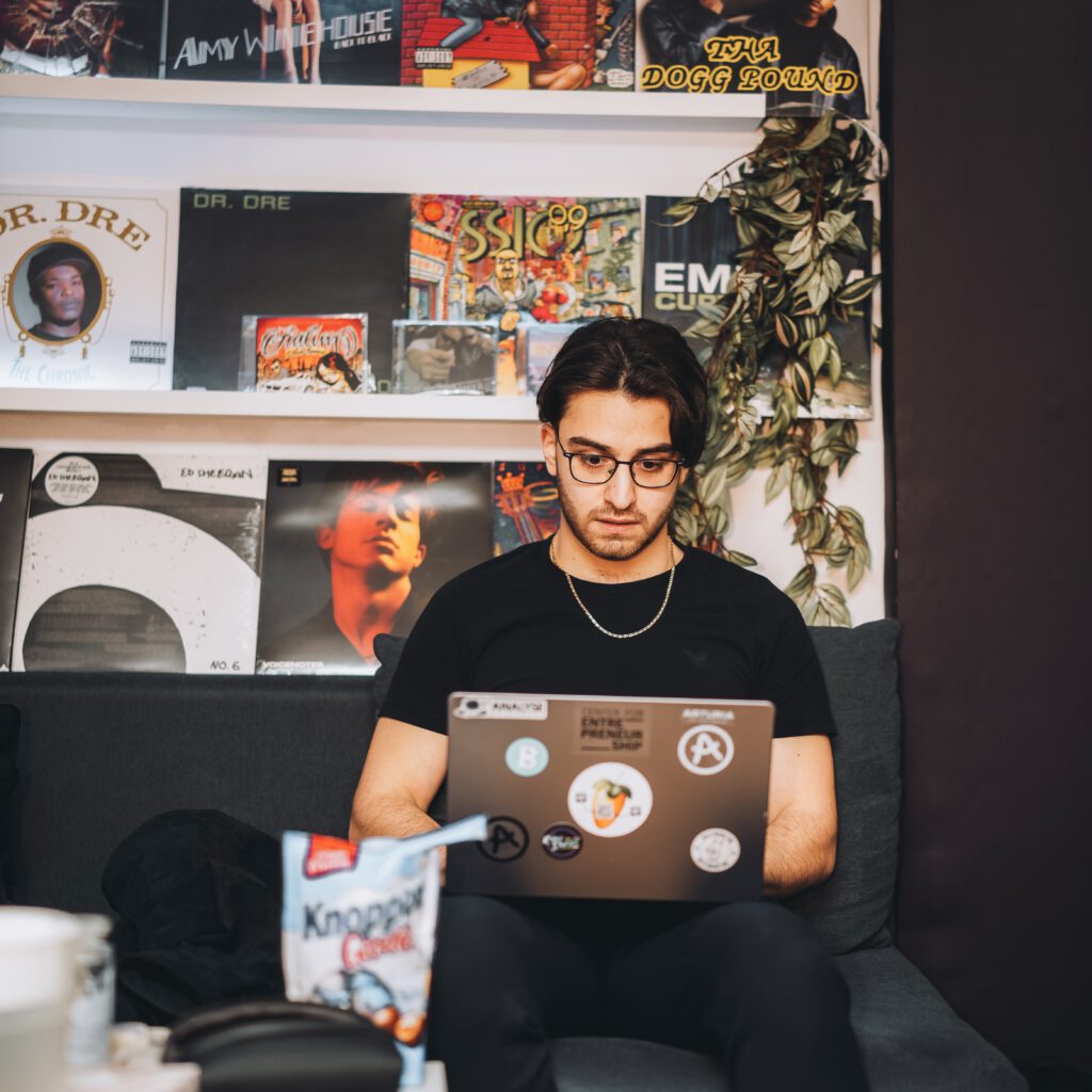BaranBeatzz arbeitet im RNMS Studio an seinem MacBook vor einer Wand voller Schallplatten